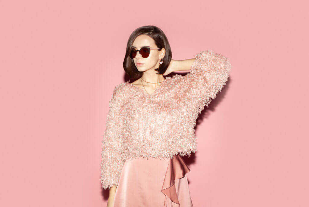 A woman poses for the camera in a fuzzy soft-pink sweater and a soft-pink skirt.