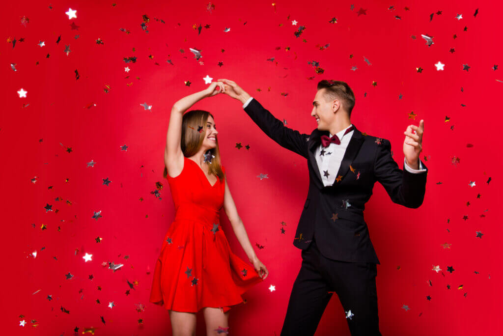 A man and woman dance together in front of a red background with confetti falling everywhere.