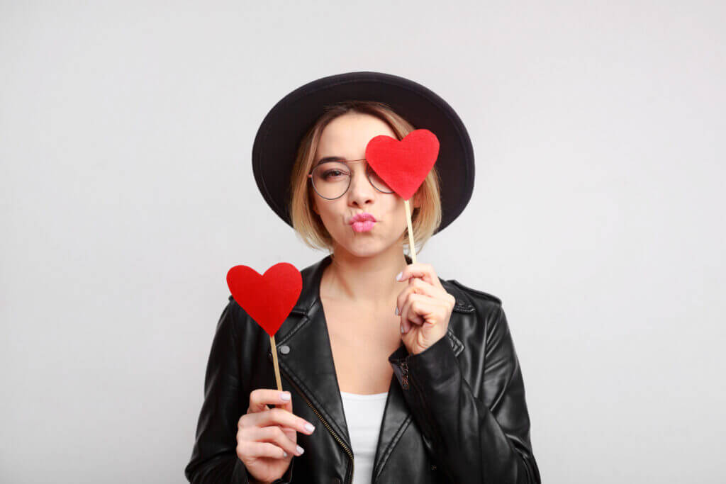 A woman in a black hat and a black leather jacket holds up two heart decorations on sticks.