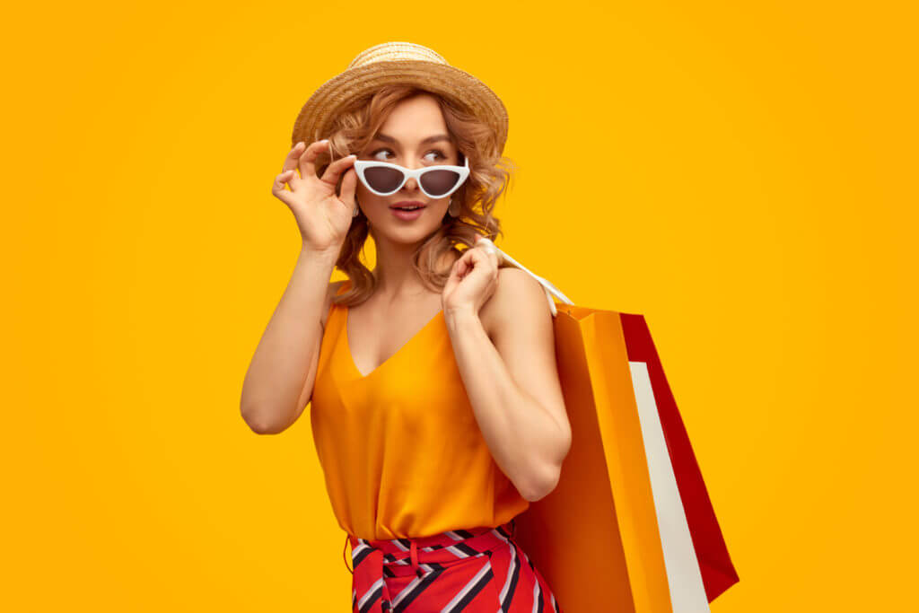 A woman in front of a yellow background poses wearing a golden yellow blouse and patterned red pants.