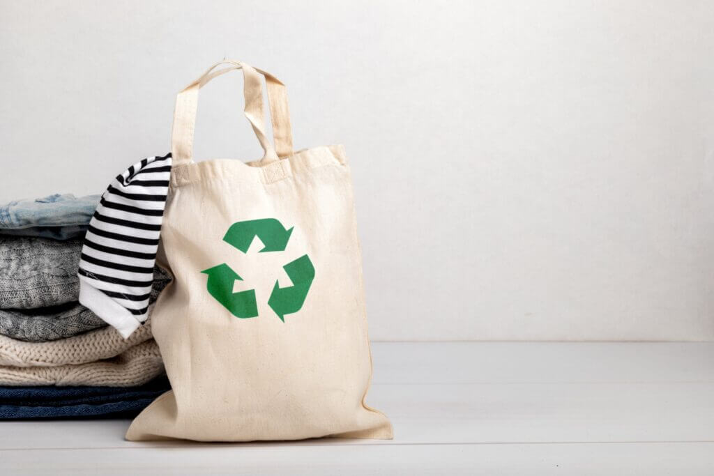 A burlap bag with a recycling symbol sits near a folded stack of clothes.